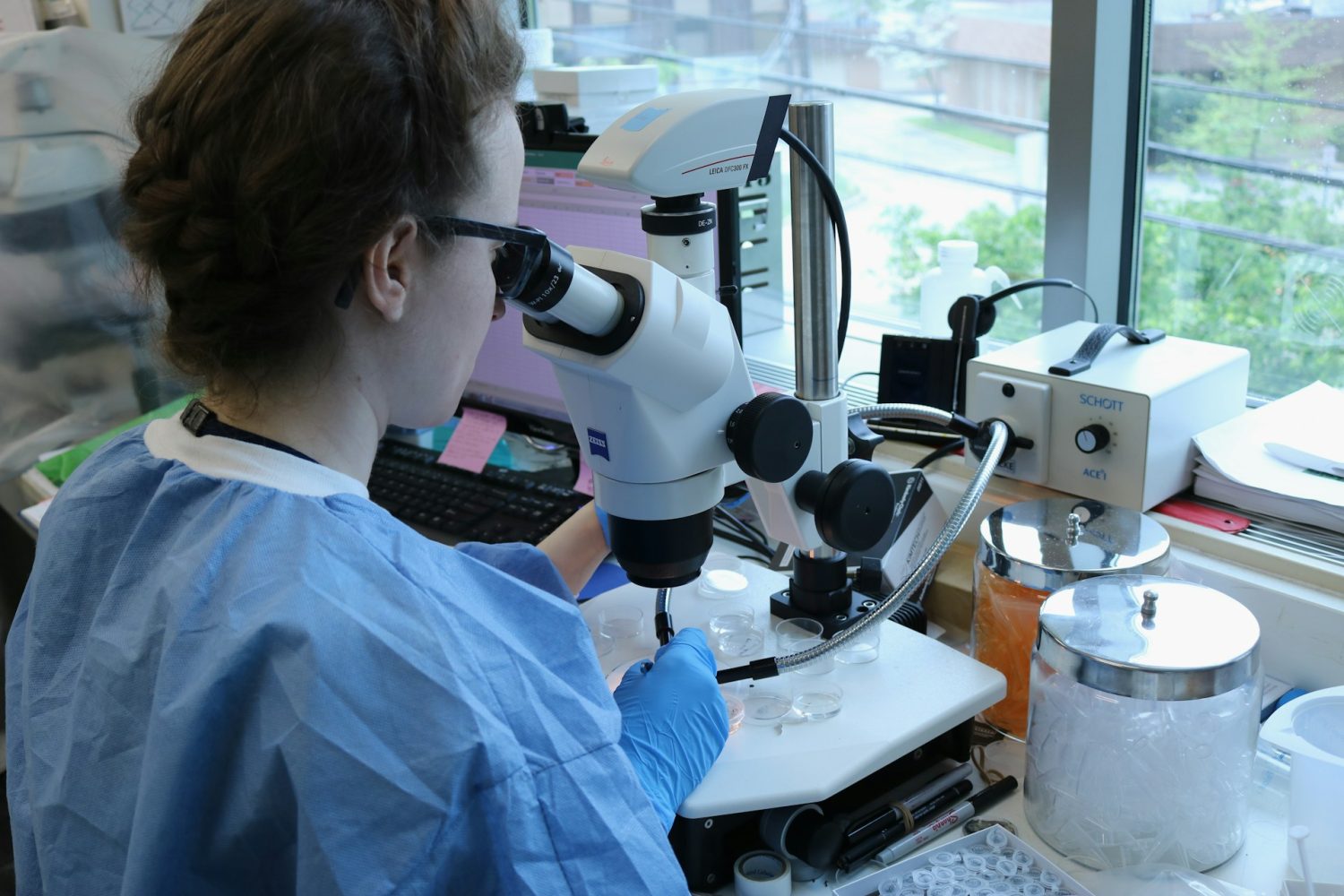 Mujer con una bata de laboratorio mirando a través de un microsocopio el análisis de ADN de AlphaGenome, la IA de Google
