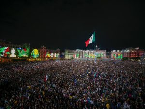 📸 Una vista panorámica impresionante del Zócalo capitalino, lleno de miles de personas que ondean banderas y disfrutan del espectáculo de luces y adornos patrios.